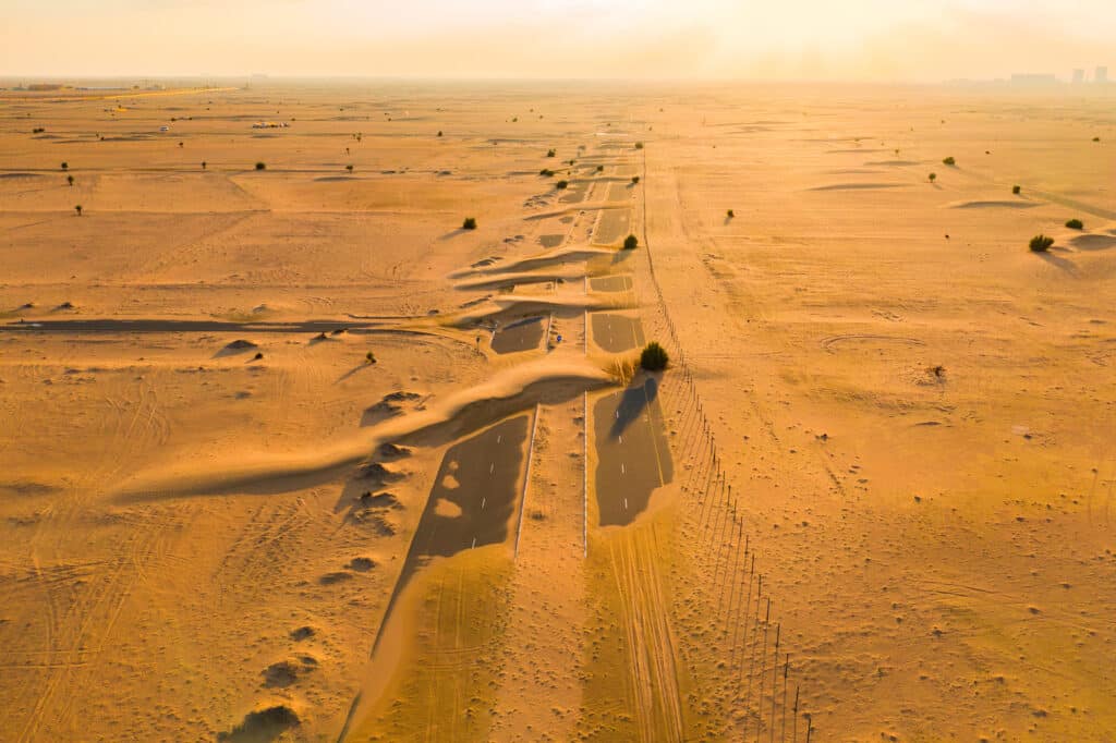 aerial view of half desert road or street with sand dune in dubai city, united arab emirates or uae. natural landscape background at sunset time. famous tourist attraction. top view.